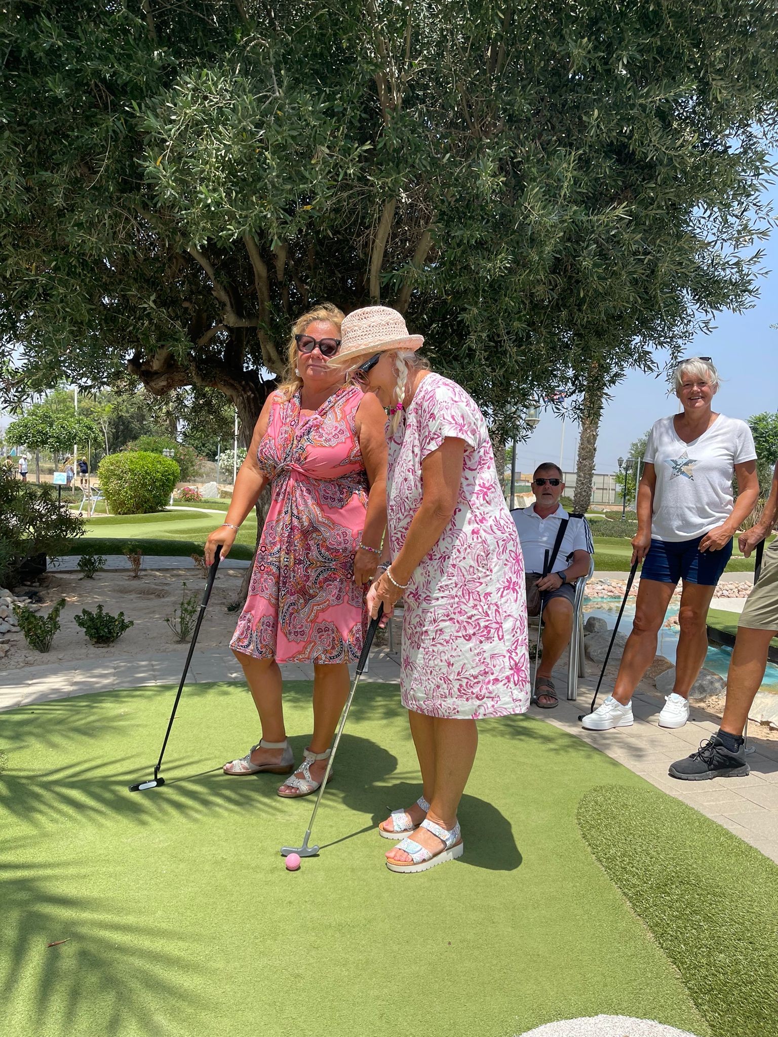 Visitors putting on the artificial grass green under an olive tree at Golf Delux